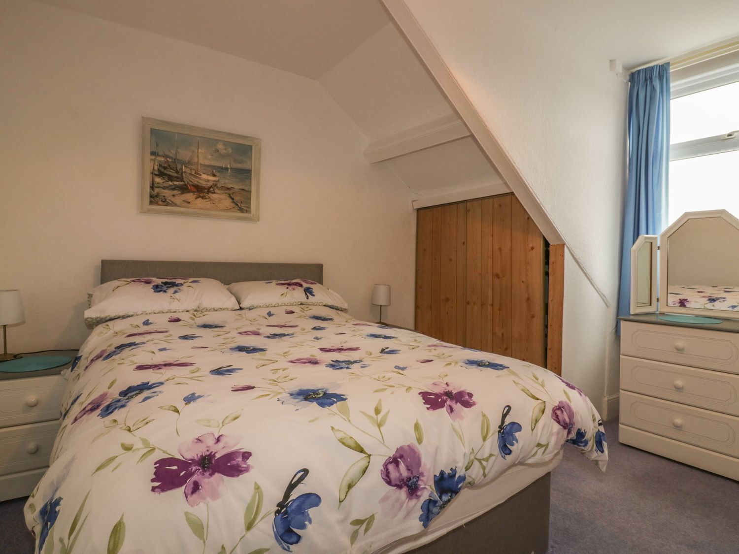 Een slaapkamer met een bed, een dressoir, een spiegel, een houten garderobe en een schilderij aan de muur.