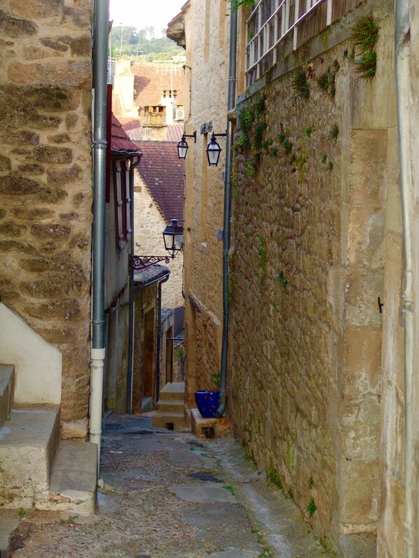 A narrow alleyway with stone walls, a metal pipe, and a blue bucket on the ground. - Studio in the Medieval Center of Sarlat (FRANREAL) (Sarlat la Caneda)