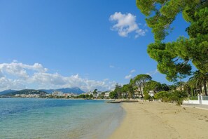 A beach with clear blue water, a sandy shore, and buildings in the background. - Penthouse 3 Bed Apartment Roof Terrace Stunning Views Puerto Pollensa, Mallorca (Port de Pollença)