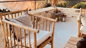 Un área de estar al aire libre con madera y vistas a un acantilado y colinas boscosas.