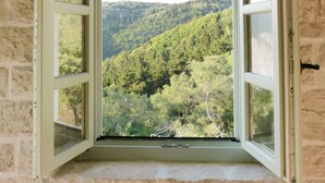 Un muro de piedra con una ventana que da a una ladera boscosa.