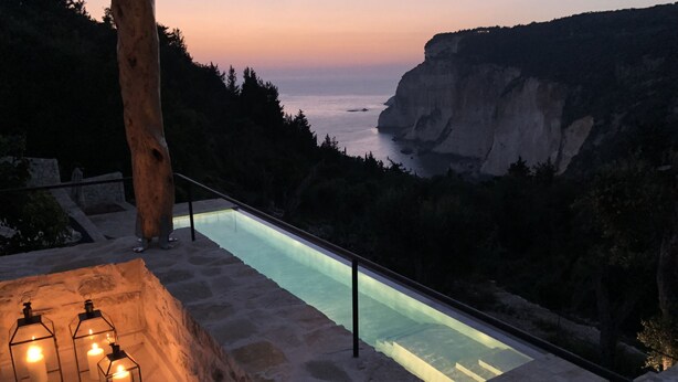 Una piscina de piedra con borde de cristal, con vistas a un acantilado y al mar.