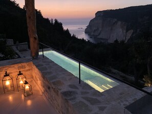 Une piscine à débordement en pierre, avec une bordure en verre, offrant une vue imprenable sur une falaise et la mer.