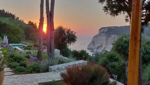 Un jardín con un sendero de piedra, una piscina y vistas al mar y acantilados.