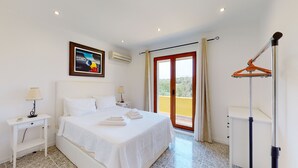 Ein Hotelzimmer mit Bett, Nachttischen, einem Gemälde, einer Klimaanlage, einem Balkon mit Aussicht und einem Wäscheständer.