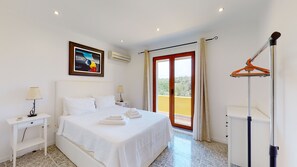 A hotel room with a bed, nightstands, a painting, an air conditioner, a balcony with a view, and a clothes drying rack.