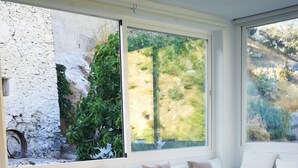 A modern living room with a white sofa, a wooden coffee table, and large windows offering a view of greenery and a stone wall. - The sky at Salares in Andalusia  (Salares)