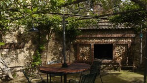 Un espacio comedor al aire libre rústico con un muro de piedra, un horno de ladrillo y sillas de metal.