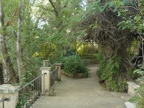 Un sendero atraviesa un jardín con un muro de piedra y una barandilla metálica a un lado.