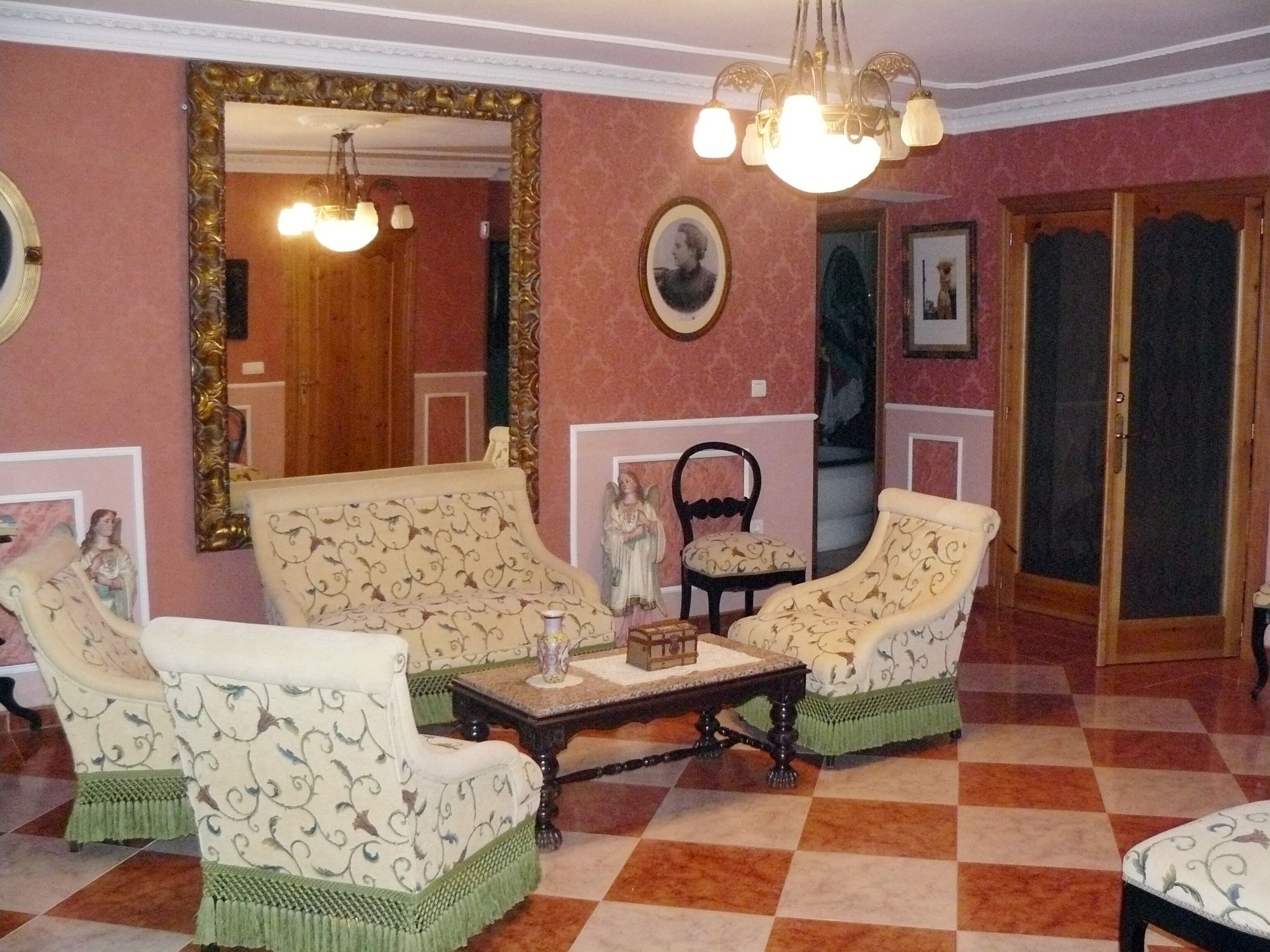 A room with two patterned armchairs, a small table, a mirror, and a chandelier.