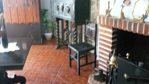 Una habitación con suelo de baldosas, un armario de madera, una silla, una chimenea con adornos y una estantería empotrada con una planta en maceta.