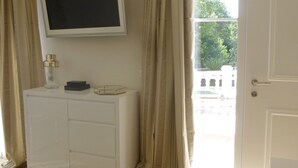 A room with a flat-screen TV mounted on the wall, a white cabinet, beige curtains, and a door leading outside. - Air-conditioned apartment with large terrace on property with swimming pool (La Roquette-sur-Siagne)