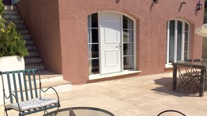 A patio with outdoor furniture, a glass table, and a white door. - Air-conditioned apartment with large terrace on property with swimming pool (La Roquette-sur-Siagne)