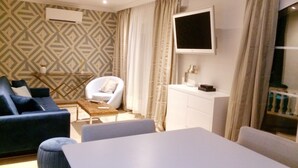 A modern living room with a sofa, armchair, ottoman, and a TV mounted on the wall. - Air-conditioned apartment with large terrace on property with swimming pool (La Roquette-sur-Siagne)