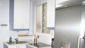 A modern kitchen with stainless steel appliances, white cabinetry, and a window with a floral pattern. - Modern apartment in Chueca Madrid (Madrid)