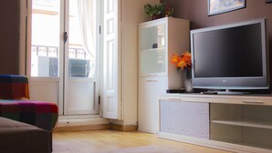 A living room with a television on a cabinet, a door leading outside, and a colorful chair. - Modern apartment in Chueca Madrid (Madrid)