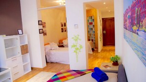 A modern hotel room with a bed, a sofa, a bookshelf, and a wall with a cityscape painting. - Modern apartment in Chueca Madrid (Madrid)