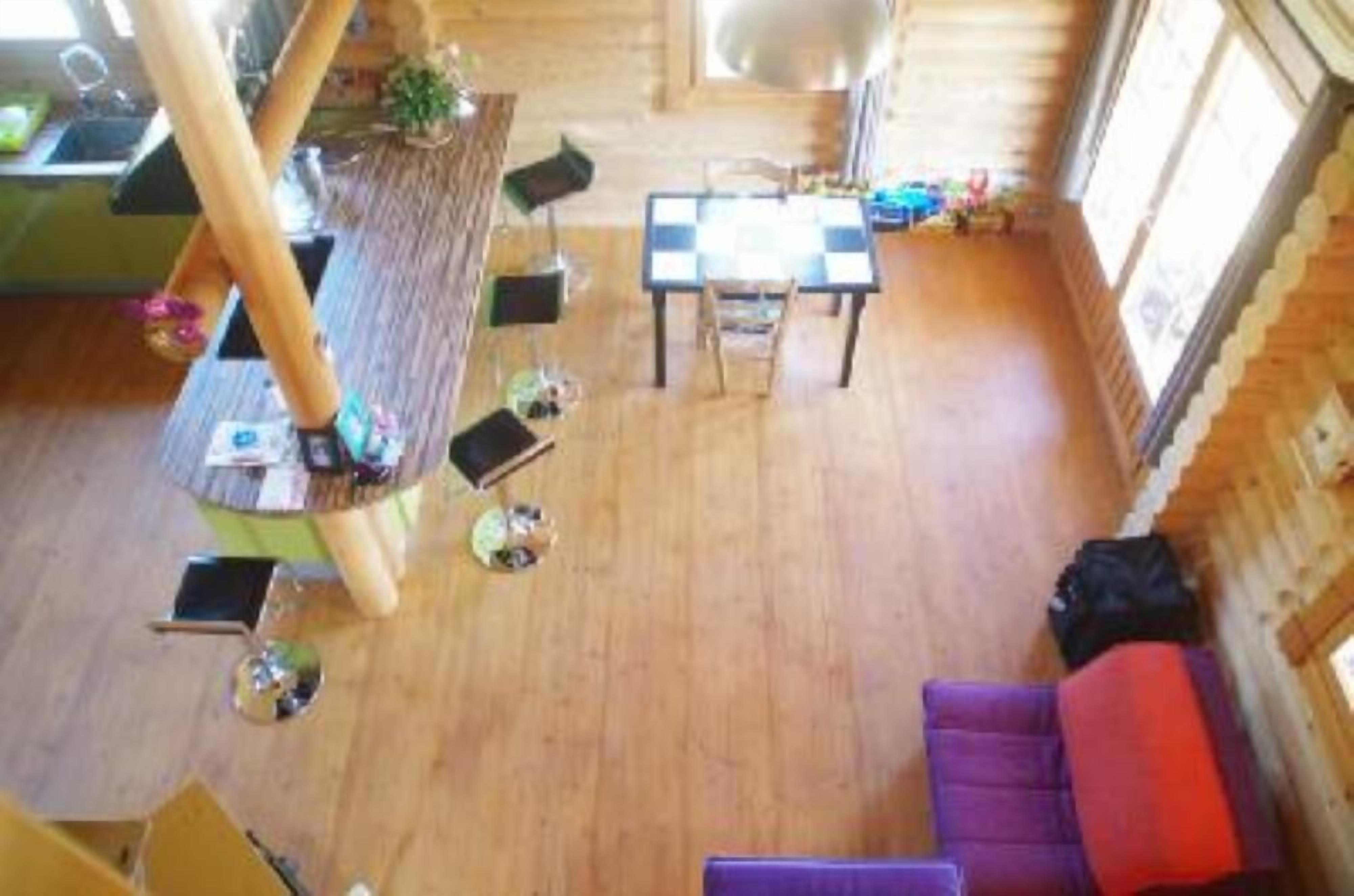 Interior d'una cabana de fusta amb taula de dinar, cadire, sofà morat i una petita cuina.