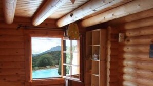 A log cabin room with a bed, a window with a view of mountains, and a wooden ceiling.