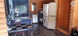 Uma cozinha compacta com pia, ventilador, mesa com toalha quadriculada e máquina de lavar.