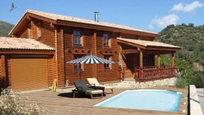 A wooden cabin with a pool, lounge chairs, and a covered deck.