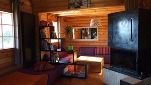A cozy log cabin interior with a sofa, a bookshelf, a coffee table, and a large black refrigerator.