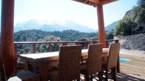 A wooden deck with a table and chairs, overlooking a mountainous landscape.