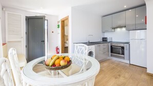 A modern kitchen with stainless steel appliances, a dining area with a round table and white chairs, and a visible fire extinguisher. - Villas Marim Jay Studio One bedroom (Olhão)