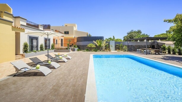 A swimming pool with lounge chairs and a covered area, surrounded by buildings and greenery. - Villas Marim Jay Studio One bedroom (Olhão)