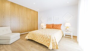 A bedroom with a large bed, a white sofa, wooden paneling on one wall, and two bedside lamps. - Villas Marim Jay Studio One bedroom (Olhão)