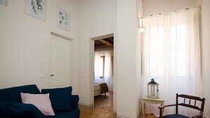 Un salon avec un canapé bleu, une chaise en bois, une petite table sur laquelle se trouve une lanterne, et une porte qui donne sur une autre pièce.
