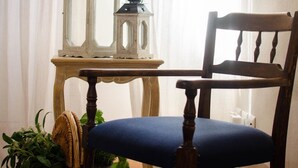 Une chaise en bois avec un coussin bleu, une petite table avec deux lanternes et un panier en osier contenant des plantes.