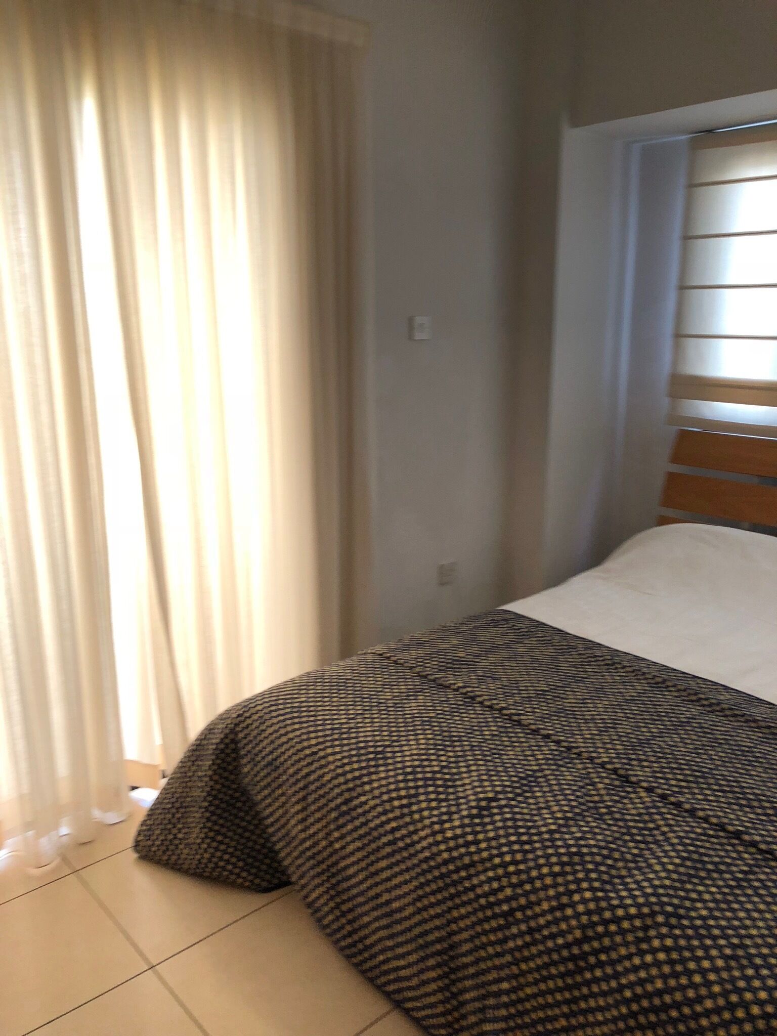 A bedroom with a bed, a window with blinds, and a curtain.