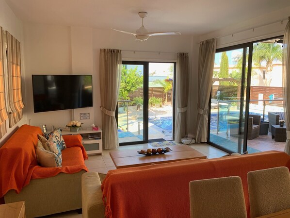 A living room with a TV, orange sofa, and a view of an outdoor pool area.