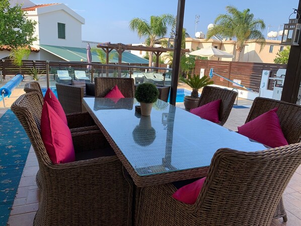 Terraza en la azotea con mobiliario de mimbre, una mesa de vidrio y vistas a una piscina y edificios.