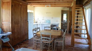 Une cuisine avec des meubles en bois, une table à manger avec des chaises, une chaise haute pour bébé et un escalier en bois.