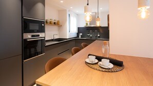 A modern kitchen with a wooden dining table, a built-in oven, and pendant lighting. - Petit Luxe l'Àtic (Terrassa) (Terrassa)