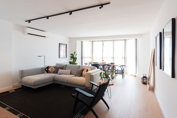 A modern living room with a sectional sofa, a dining area with a table and chairs, and large windows allowing natural light. - Petit Luxe l'Àtic (Terrassa) (Terrassa)
