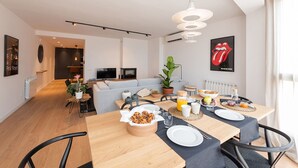 A modern living room with a sofa, a dining table set for breakfast, and a kitchen area in the background. - Petit Luxe l'Àtic (Terrassa) (Terrassa)