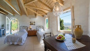 Une chambre rustique avec deux lits, une table en bois sur laquelle sont disposés des fruits et un vase, et une vue sur la campagne.