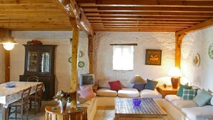 Un intérieur rustique avec un sol en pierre, des meubles en bois, un ensemble de canapés, une table à manger et un téléviseur.