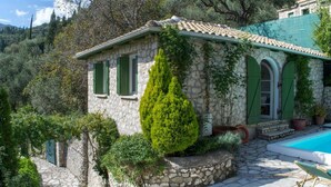 Une maison en pierre avec une piscine, des volets verts et un jardin bien entretenu.