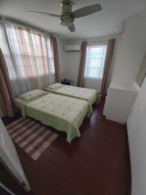 A room with two beds, a ceiling fan, and a window with curtains.