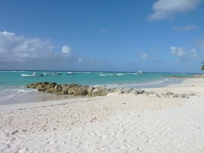 Ein Strand mit weißem Sand und türkisblauem Wasser. Mehrere Boote liegen im Wasser vor Anker.