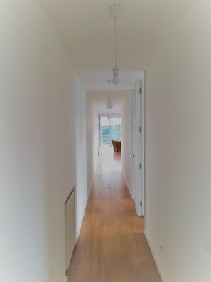 Un pasillo estrecho con suelo de madera y paredes blancas que conduce a una habitación con vistas a zonas verdes.