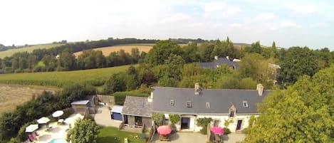 A large house with a swimming pool, surrounded by lush greenery and fields.