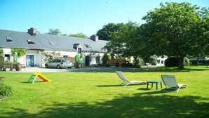 A house with a sloped roof, a car parked in front, and a grassy lawn with two lounge chairs. - House with heated indoor swimming pool  (Évellys)