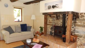 A cozy living room with a stone fireplace, a sofa, a coffee table, and a window with blinds. - House with heated indoor swimming pool  (Évellys)