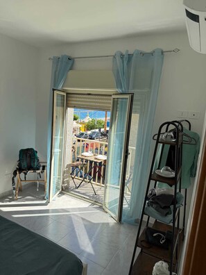 Una habitación con cama, una silla, una mesa con sillas, una ventana con cortinas y vistas a la calle.