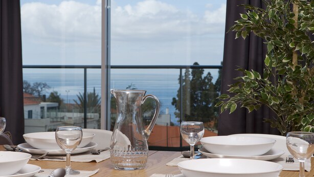 A dining table set with white plates, bowls, and glasses, with a pitcher and a potted plant. - Funchal Carvalhal Old Town (Funchal)